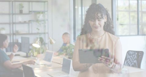Standing woman holding tablet in bright coworking office with laptops and greenery
