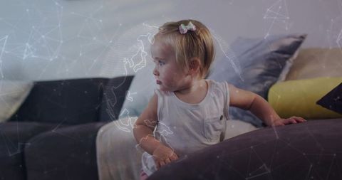 Toddler exploring connected world: curious girl leaning on couch with digital globe overlay