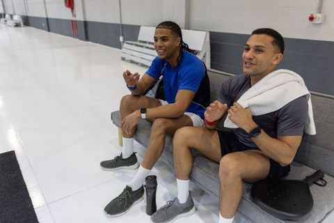 Diverse male friends relaxing and chatting on gym bench after workout with towel and water bottle