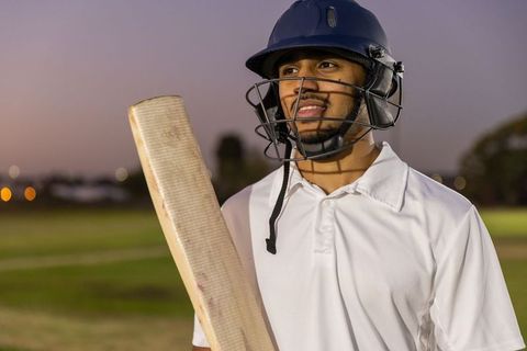 Indian cricketer standing with worn bat wearing navy helmet during twilight practice