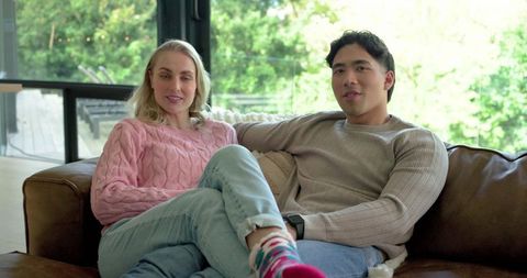 Couple relaxing on leather sofa in sunlit living room wearing cozy sweaters and jeans