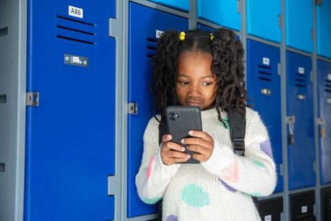 Young student near school lockers using smartphone