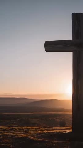 Vertical video of sun rising behind rustic wooden cross on hilltop at golden dawn
