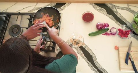 Overhead view african american woman stirring shredded carrots on gas stove for healthy meal prep