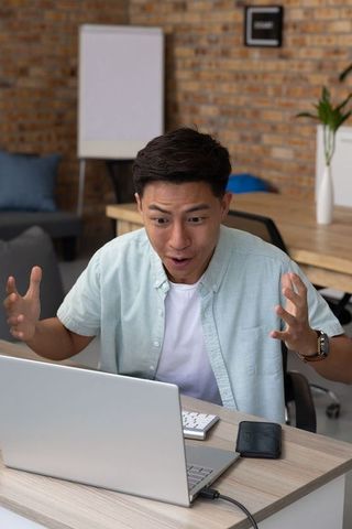 Surprised asian man reacting to laptop in modern office