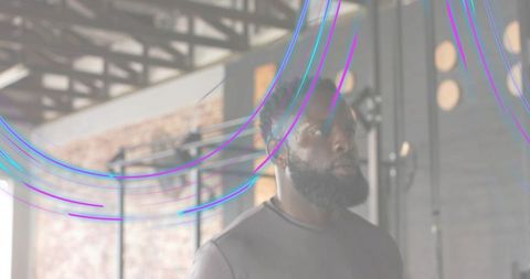 Bearded man standing in industrial gym with neon light streaks and focused expression