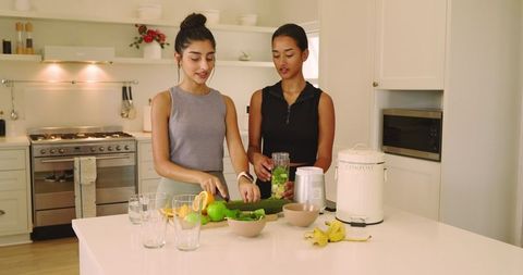 Diverse friends making healthy green smoothies in modern kitchen