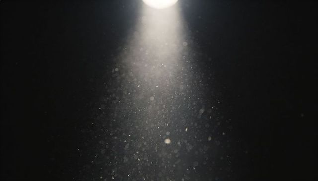 Overhead spotlight illuminating floating dust motes in dark studio with conical beam