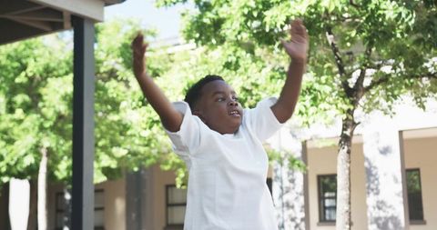 Joyful child raising arms while playing in sunlit school courtyard