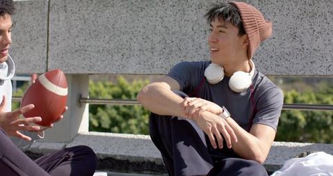 Rooftop friends relaxing with headphones and football during sunny outdoor hangout