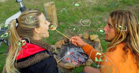 Couple sharing roasted marshmallow by campfire, sitting cozy outdoors, embracing romance