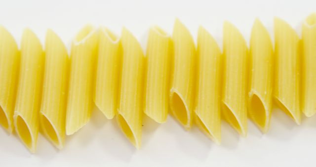 Penne pasta aligned in a row on a white background, showcasing its tubular shape and texture. Useful for food blogs, recipe websites, culinary magazines, and dietitian promotions. Ideal for illustrating articles on Italian cuisine, ingredients, and healthy eating habits.