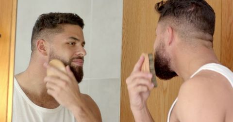 Bearded man grooming with wooden brush in modern bathroom