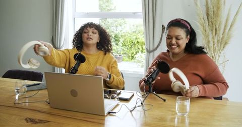 Diverse female co-hosts recording lively podcast around wooden table in bright home studio
