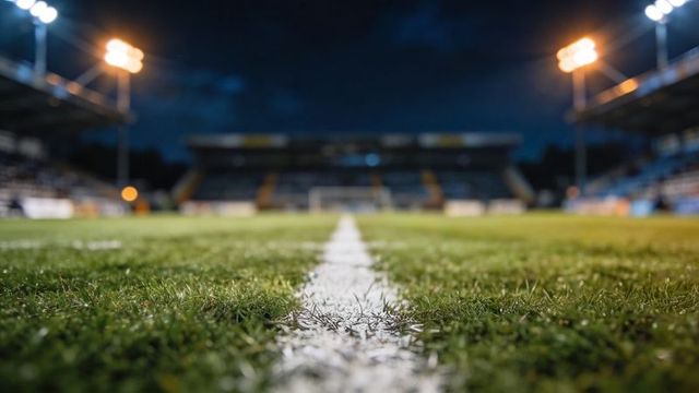 Running center line leading across football pitch toward goal under stadium floodlights