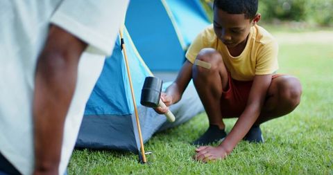 African american father and son hammering tent stake in backyard camping outdoor bonding