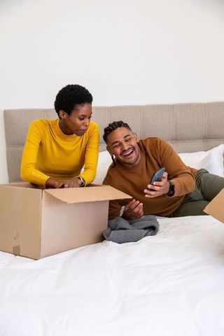 Diverse couple unpacking boxes in bedroom with relaxed atmosphere