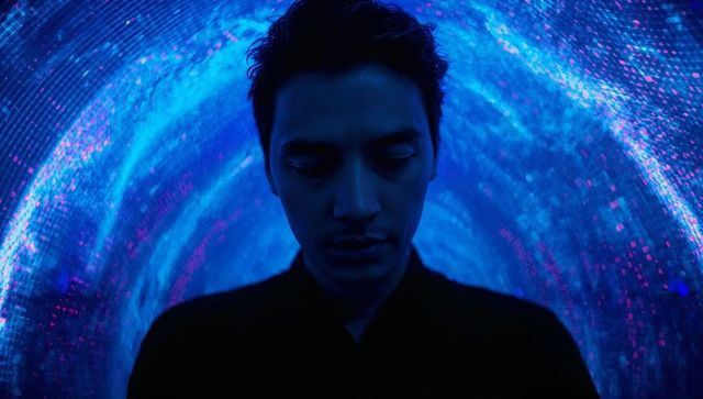 Contemplative man standing in neon blue LED tunnel with magenta particle lights