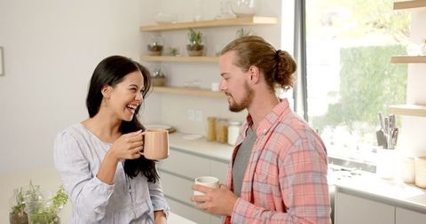 Happy multicultural couple enjoys coffee together at home kitchen