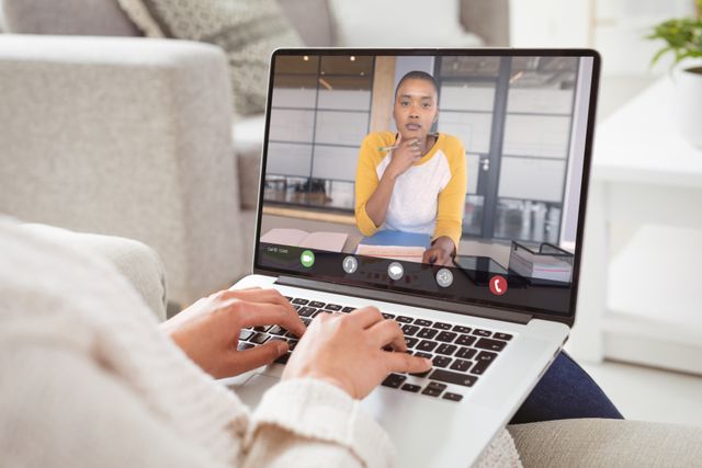African american businesswoman with hand on chin during video call with caucasian female colleague. unaltered, work from home, business, wireless technology, working, teamwork and office concept.