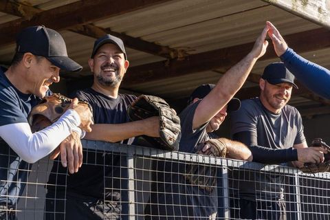 Veteran baseball players celebrating and high-fiving in dugout while smiling with gloves