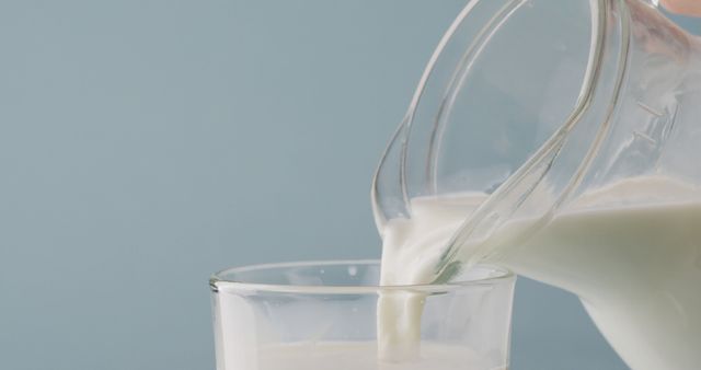 Clean, simple image of milk being poured from a clear pitcher into a glass on plain backdrop. Ideal for use in advertisements, health and nutrition articles, dairy products promotions or breakfast themes.