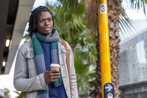 African american commuter holding coffee while waiting at urban stop with palm trees
