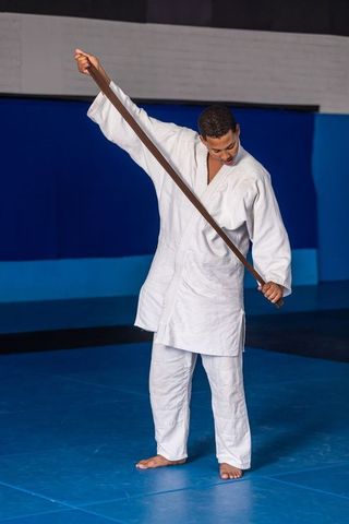 Martial artist in kimono holding belt on blue mat, strength and discipline