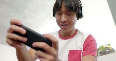 Asian teen enjoying mobile game with headphones