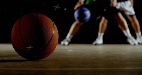 Resting orange basketball on hardwood court with players dribbling in background