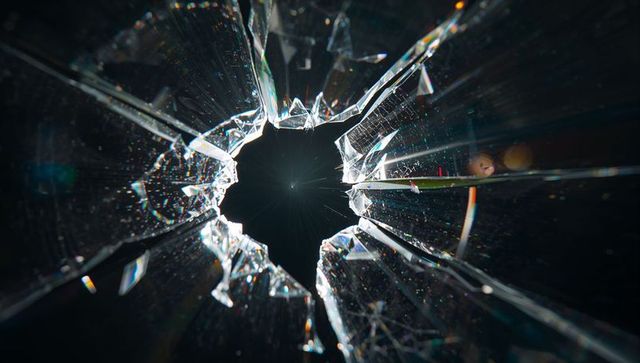 Shattered glass hole radiating shards with prismatic light, dust and radial fracture