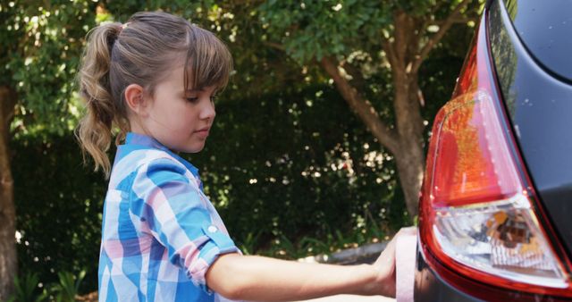 A young Caucasian girl is focused on washing a car outdoors, with copy space. She appears to be engaged in a common household chore, contributing to family responsibilities.
