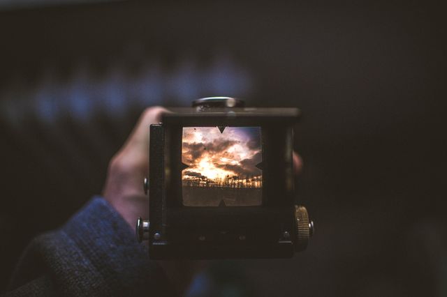 This image showcases a vintage camera viewfinder capturing a beautiful and dramatic sunset. Ideal for use in blogs or marketing materials focused on photography, nature, technology, or nostalgia. It can also serve as an inspirational visual for creative projects highlighting picturesque landscapes and the art of photography.