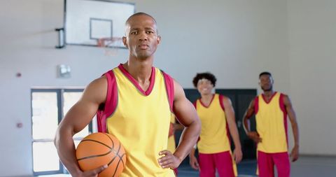 Confident Basketball Player Holding Ball with Teammates in Gym