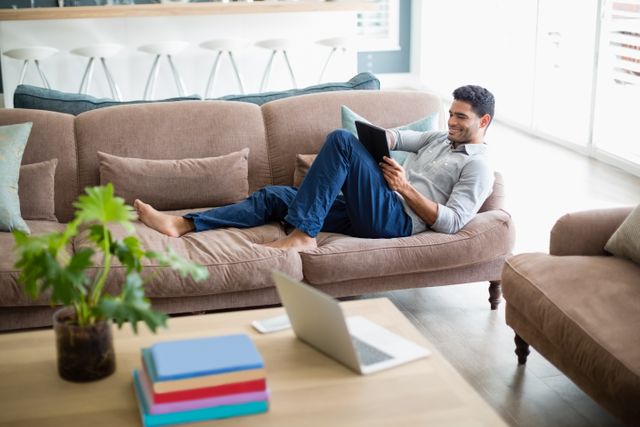 Man sitting on sofa and using digital tablet in living room at home