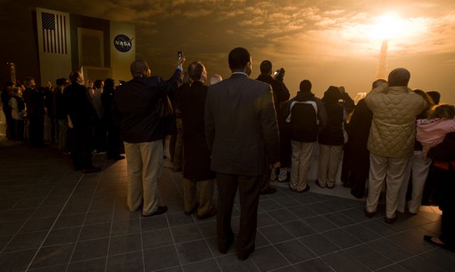 Crowd watching space shuttle Endeavour launching at sunrise from Kennedy Space Center. Image captures excitement and awe of space exploration. Ideal for articles on NASA missions, space exploration history, or public reactions to space launches.