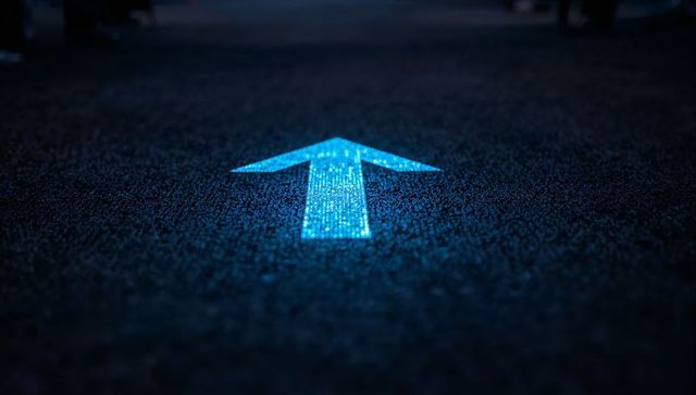 Glowing cyan arrow on asphalt guiding forward direction at night with pixelated led glow