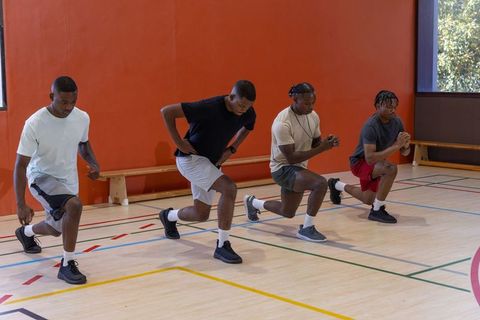 African american men performing forward lunges in indoor gym for group fitness training