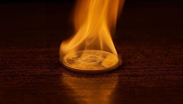 Burning bitcoin coin on dark wood representing cryptocurrency crash and financial risk