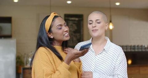 Diverse friends sharing smartphone playlist in cozy cafe, mustard sweater and shaved head