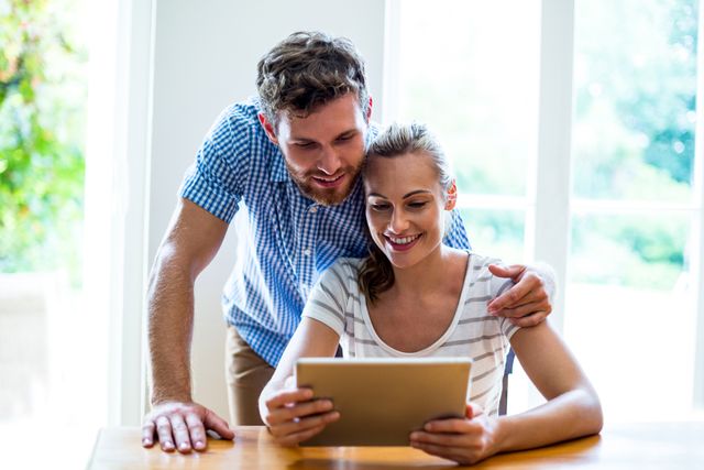 Couple smiling while using a digital tablet at home. Ideal for depicting modern technology use, happy relationships, and home lifestyle. Suitable for advertisements, blog posts, and articles about technology, family life, or home activities.