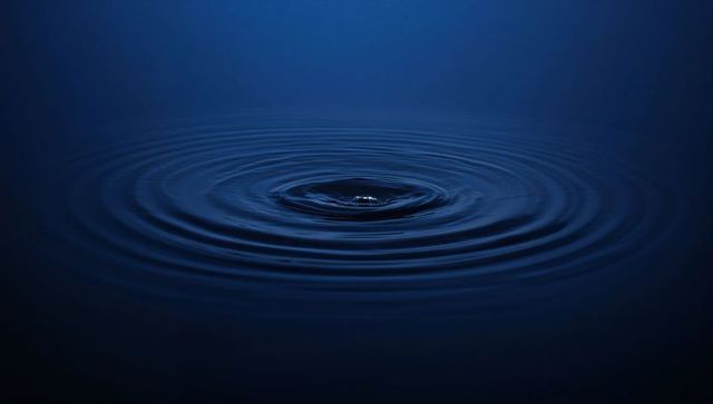 Concentric water ripples creating calm dark blue minimalist background with central droplet