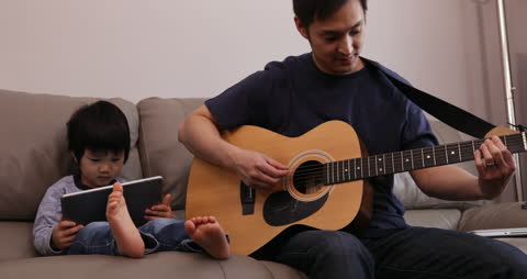 Father Playing Guitar While Son Engages with Tablet at Home