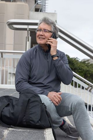 Senior asian man sitting on urban steps talking on smartphone with backpack and smartwatch