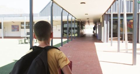 Student with Backpack Stands in Sunlit School Corridor