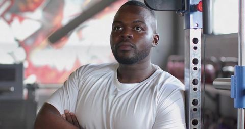 Confident man standing with arms folded wearing white t-shirt looking up by power rack