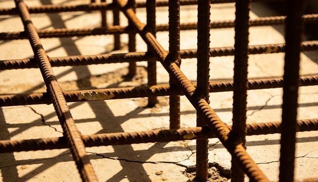 Rusted rebar grid casting strong shadows on cracked concrete slab detail