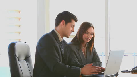 Professionals Collaborate on Project with Laptop at Desk in Office