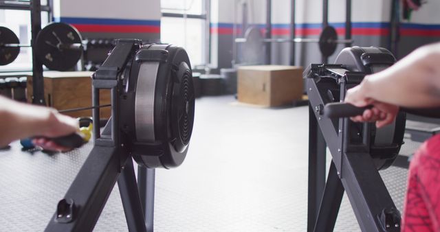 Image of rear view of two diverse women on rowing machines working out at a gym. Exercise, fitness and healthy lifestyle.