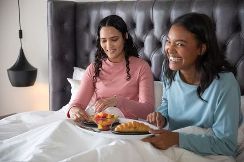 Diverse friends sharing cozy bed breakfast with laughter
